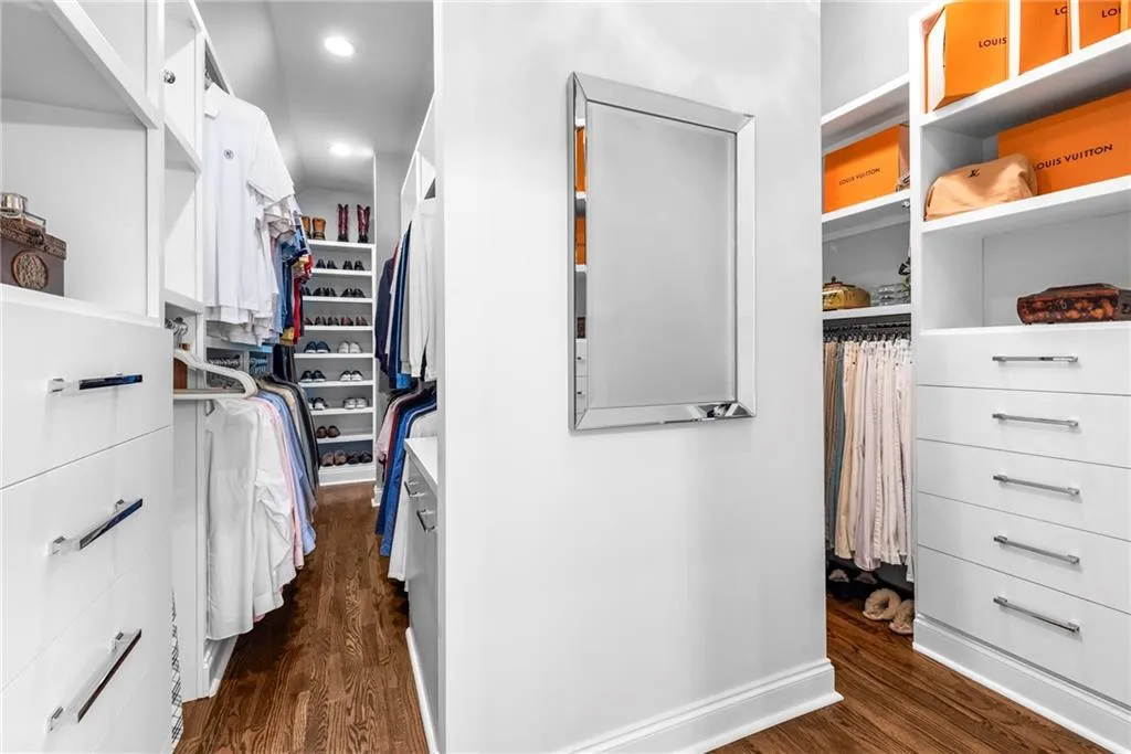 Primary walk-in closet with custom floor-to-ceiling double-sided design, including cabinet drawers, two laundry pull outs, additional shelving, hanging space, and shoe shelves. Hardwood flooring. Primary walk-in closet with custom floor-to-ceiling double-sided design, including cabinet drawers, two laundry pull outs, additional shelving, hanging space, and shoe shelves. Hardwood flooring.