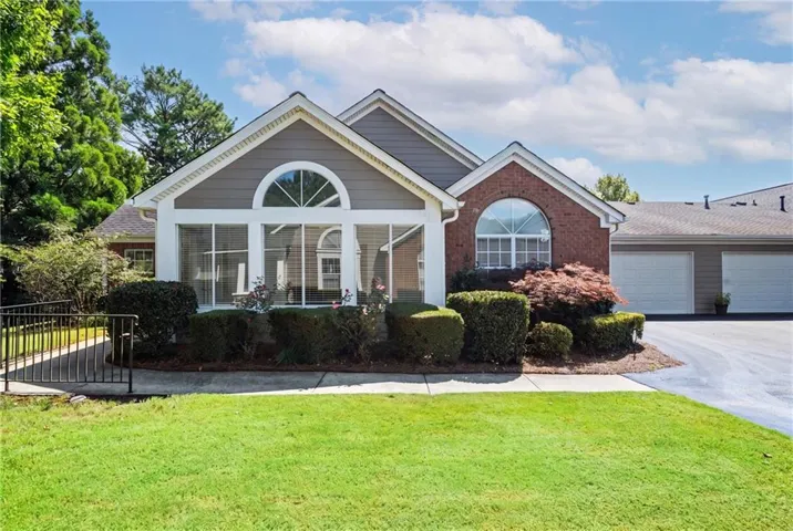 Exterior featuring a brick facade with an arched window, a spacious sunroom with large windows, and a well-maintained lawn