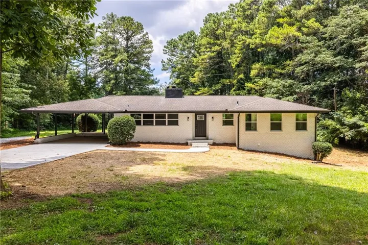 Ranch-style residence featuring a white brick exterior, dark brown front door, and a covered carport