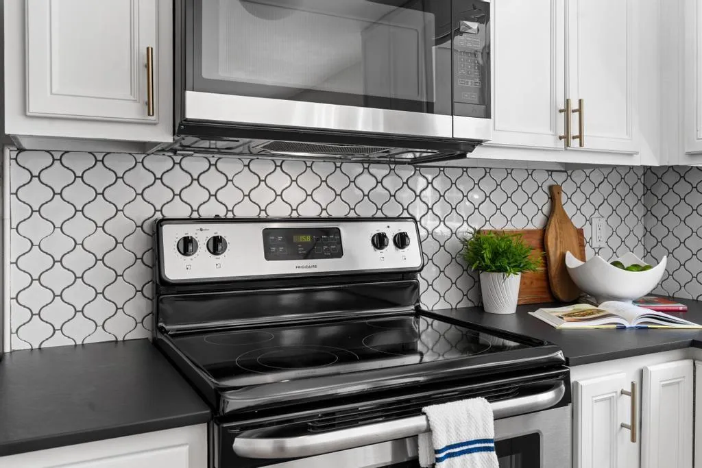 Kitchen featuring stainless steel appliances, dark countertops, white cabinetry, and tasteful backsplash