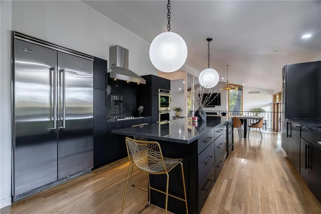 Kitchen featuring a large island, stainless steel appliances, wall chimney range hood, light hardwood / wood-style floors, and decorative light fixtures