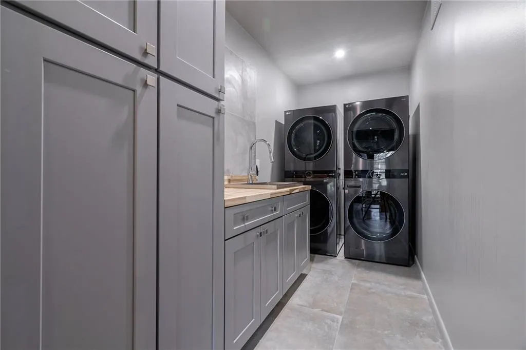 Washroom with sink, cabinets, and stacked washer and clothes dryer