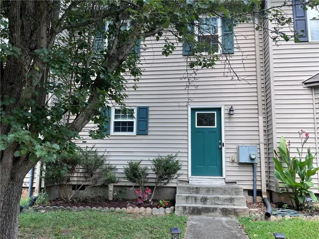 Light-colored siding exterior with a teal entry door, decorative window shutters, and a concrete pathway
