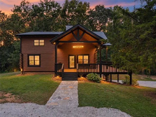 Wood-sided exterior with a covered porch, outdoor deck, flagstone walkway, and mature trees