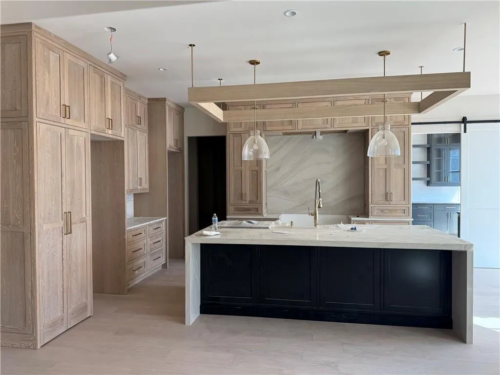 Kitchen featuring light stone counters, a large island, dual tone cabinetry, a barn door, and light wood-type flooring