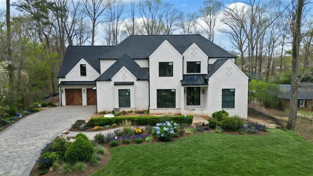 View of front of home featuring a standing seam roof, decorative driveway, a front lawn, brick siding, and a shingled roof