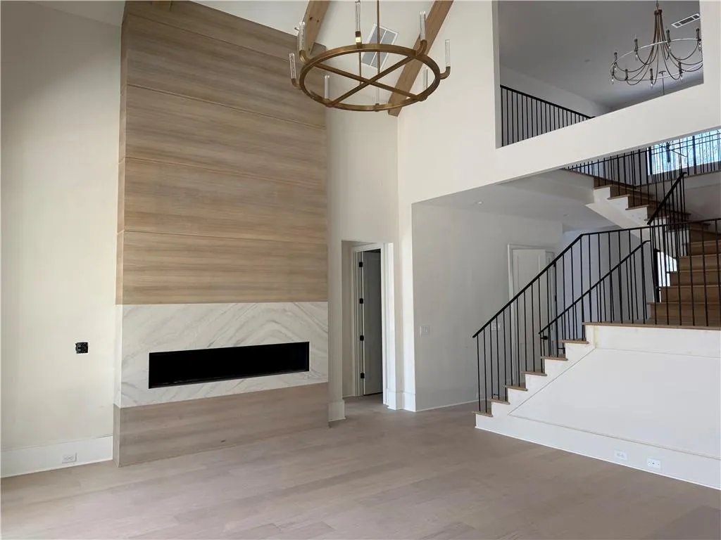 Unfurnished living room with suspended lighting, a premium fireplace, light wood finished floors, and a high ceiling