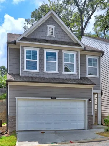 Two-story gray siding exterior with white trim, gable roof, attached garage, and stone veneer accents