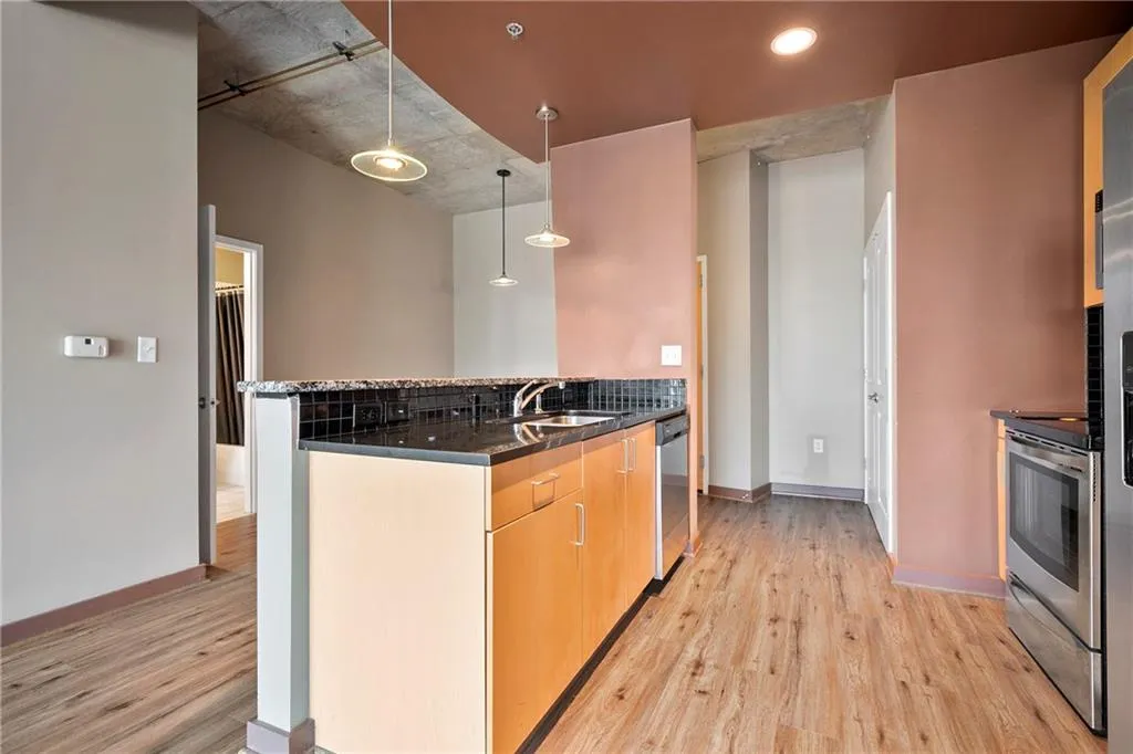 Kitchen featuring light wood-style floors, a sink, dishwasher, decorative light fixtures, and baseboards