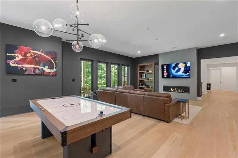 Spacious room featuring light wood-finish flooring, dark accent walls, and a modern chandelier