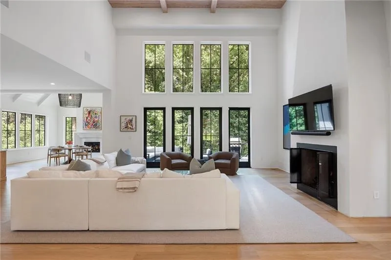 Double-height living space featuring exposed wood ceiling beams, a striking fireplace with an integrated media niche, and light wood-finish flooring
