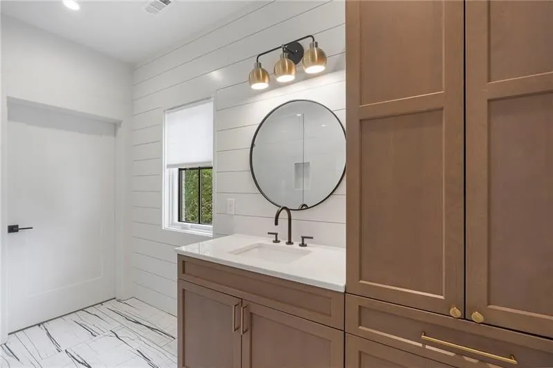 Bathroom featuring a single vanity with stone countertop, round mirror, and black hardware