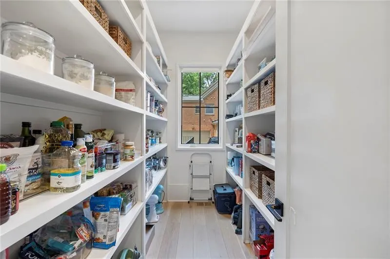 Walk-in pantry with extensive built-in shelving, natural wood-finish flooring, and natural light from the window