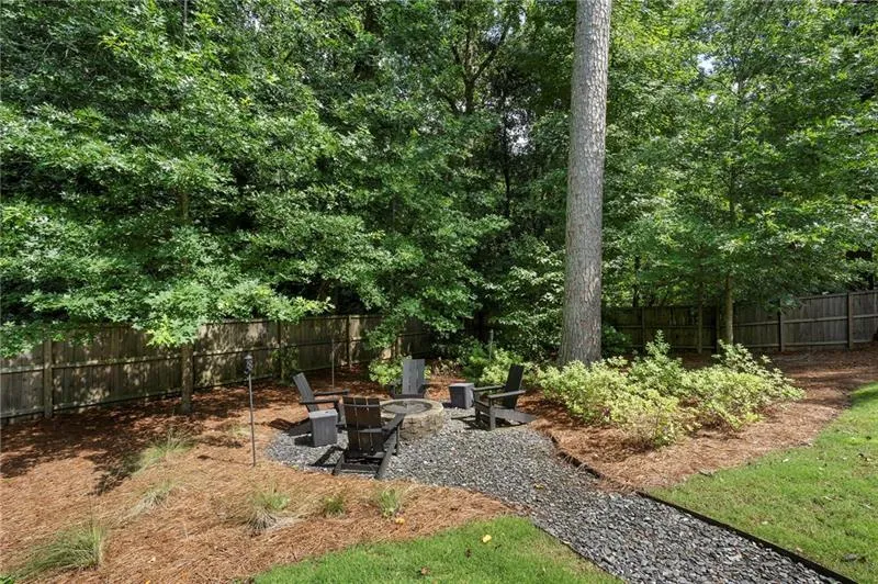 Outdoor entertaining area featuring a fire pit surrounded by Adirondack chairs, a gravel pathway, and mature trees