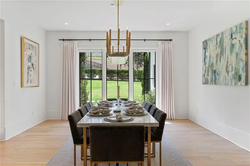Dining area featuring a contemporary chandelier, light wood-finish flooring, white baseboards, and large black-framed windows overlooking a green lawn