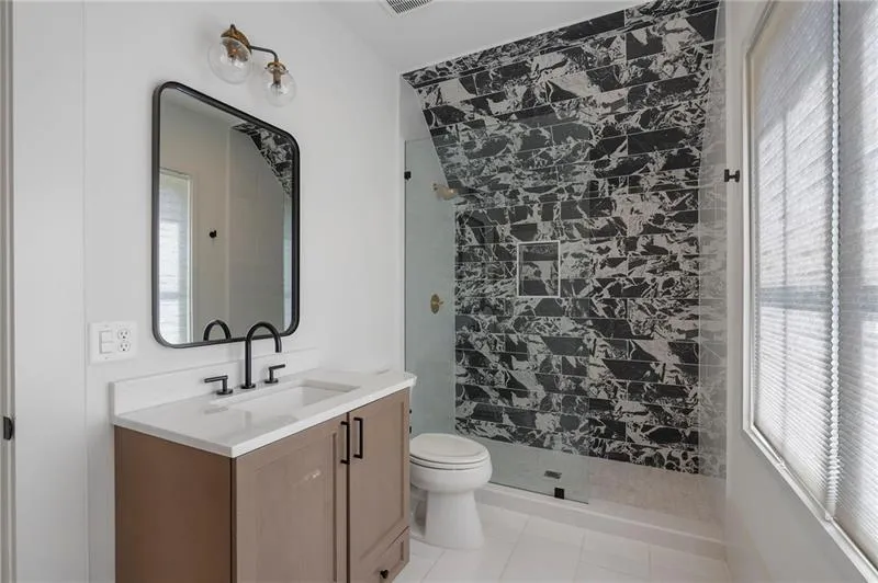 Bathroom featuring a glass-enclosed shower with black and white patterned tile, a single vanity with a white countertop and dark wood-finish cabinetry, a rectangular framed mirror, and matte black fixtures
