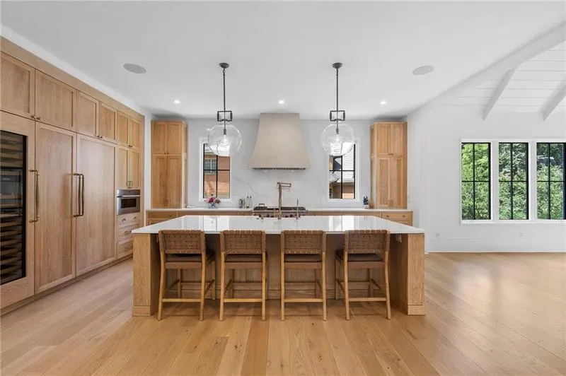 Open-concept kitchen featuring an oversized island with a quartz countertop, integrated panel-front appliances, wood-finish flooring, and a vaulted ceiling
