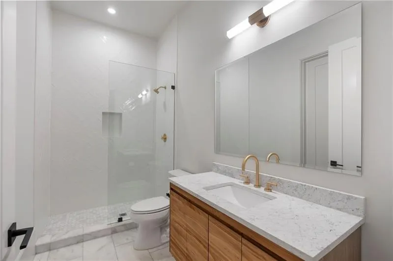 Modern bathroom featuring a frameless glass shower enclosure, a white tiled shower surround with a built-in niche, and a light wood-finish vanity with a white countertop and undermount sink