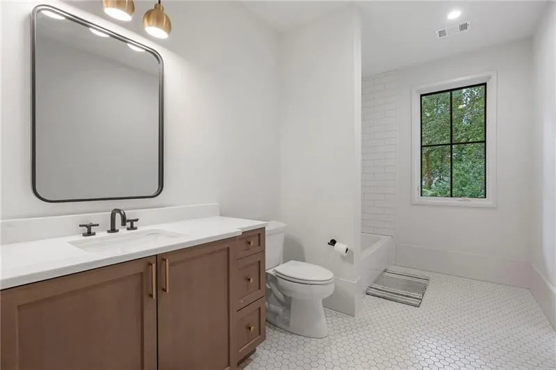 Bathroom featuring a wood-finish vanity with a white countertop, matte black fixtures, a rectangular mirror, and white hexagonal floor tiles