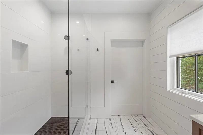 Contemporary bathroom featuring a glass-enclosed shower with a recessed niche, shiplap accent wall, and a window with a cellular shade