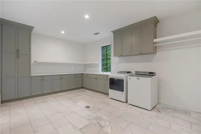 Spacious utility room featuring extensive built-in cabinetry, durable tile flooring, a functional sink, subway tile backsplash, and a dedicated hanging rack
