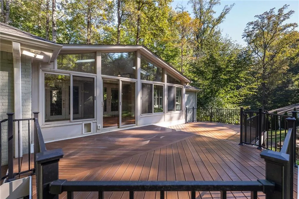 Expansive composite deck featuring black metal railings, floor-to-ceiling windows, sliding glass doors, and a brick exterior