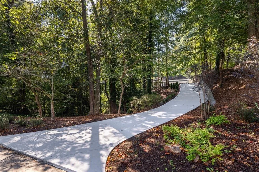 Paved concrete driveway framed by mature trees, established landscaping, and natural woodland terrain