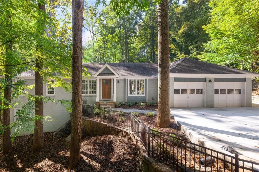 Single-story exterior featuring painted brick siding, a two-car garage, multi-pane windows, a covered entry with a gable portico, and tiered stone retaining walls with metal fencing