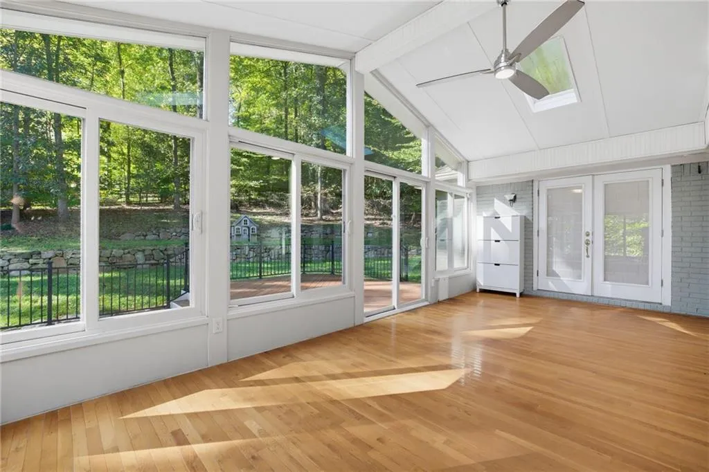 Sunroom featuring floor-to-ceiling windows, wood-finish flooring, vaulted ceiling with a skylight, ceiling fan, and double glass-panel doors