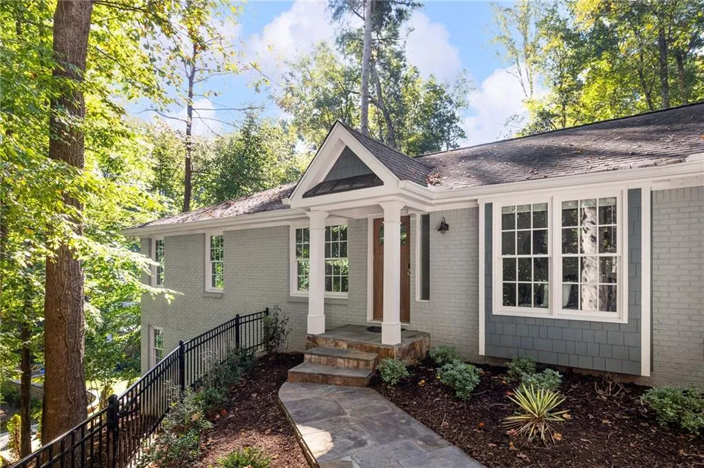 Painted brick exterior with shingle siding, covered front entryway with gabled roof, stone-paved walkway, and metal railing
