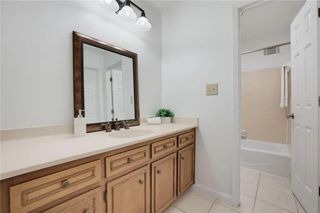 Bathroom featuring a wood-finish vanity with a solid-surface countertop, an integrated sink, a framed mirror, and tile flooring