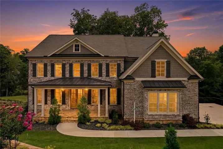 Two-story residence featuring brick and shake siding, a covered front porch, dark window shutters, a paved walkway, and manicured landscaping