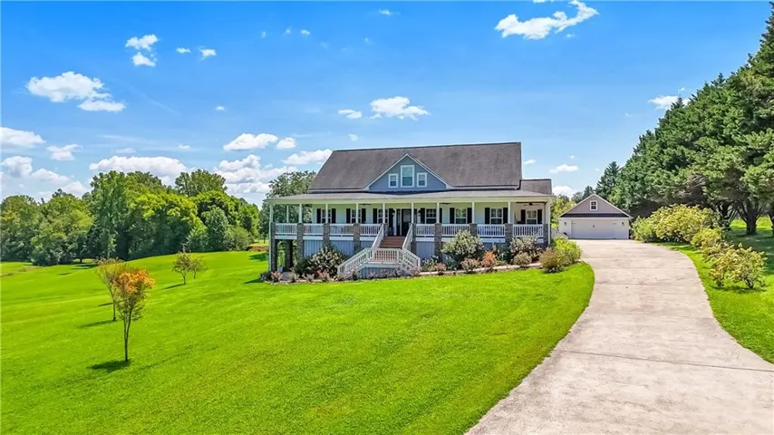 Two-story residence with a wraparound porch, featuring a detached garage, concrete driveway, and expansive green lawn