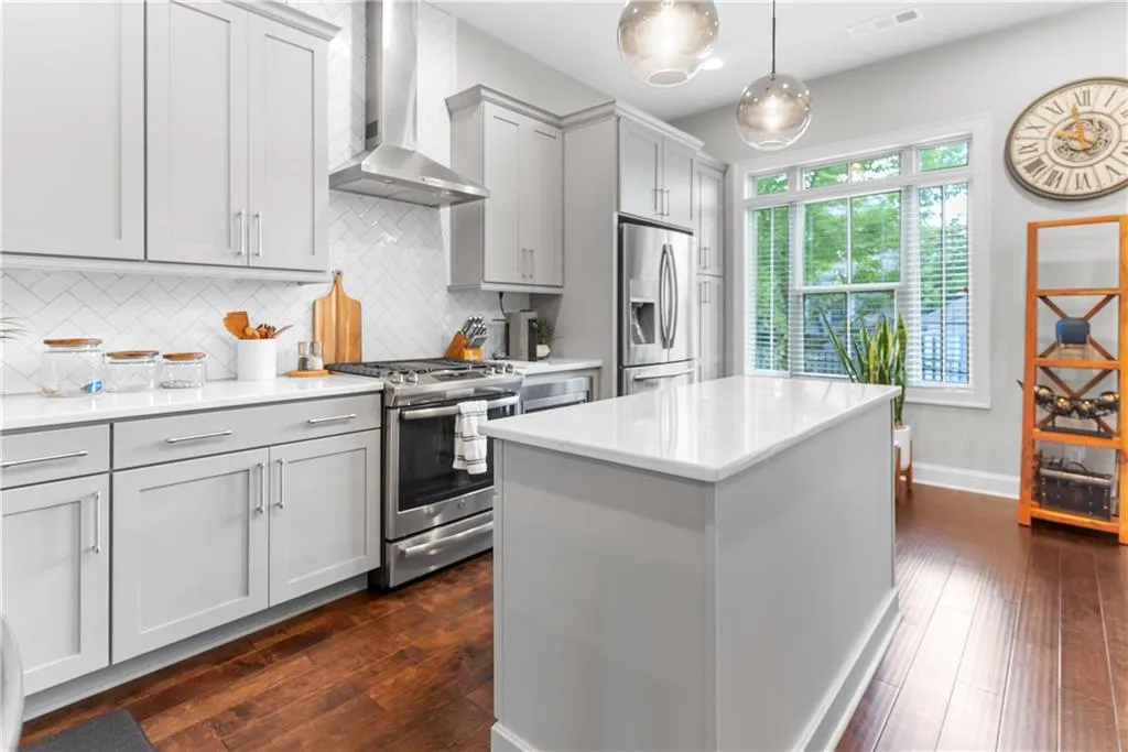 Kitchen with stainless steel appliances, tasteful backsplash, decorative light fixtures, dark wood-type flooring, and wall chimney range hood