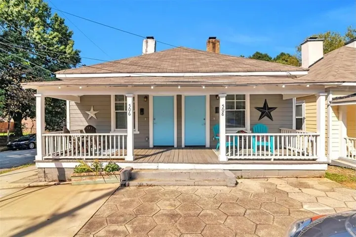 Covered front porch with white railing, wood-finish porch flooring, and light blue entry doors