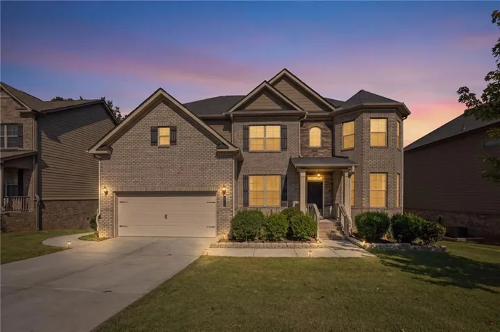 Brick façade with stone accents, covered front entry, attached garage, and mature landscaping