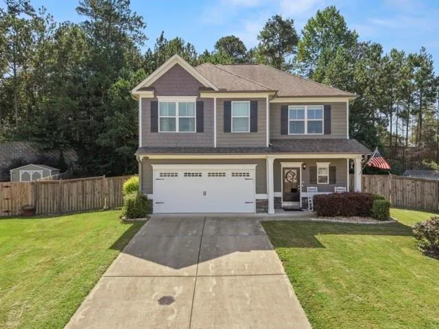 Two-story residence featuring a covered front porch, attached garage, and a fenced backyard with a storage shed