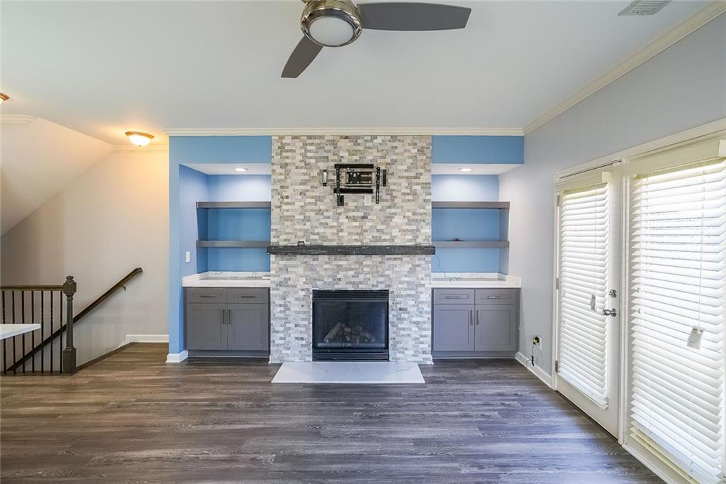 Unfurnished living room with dark hardwood / wood-style flooring, ceiling fan, a stone fireplace, and ornamental molding