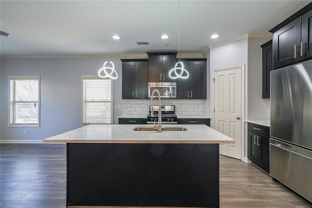 Kitchen with pendant lighting, hardwood / wood-style flooring, light stone countertops, and stainless steel appliances