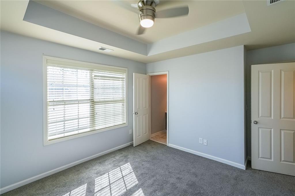 Unfurnished bedroom with dark colored carpet, a tray ceiling, and ceiling fan