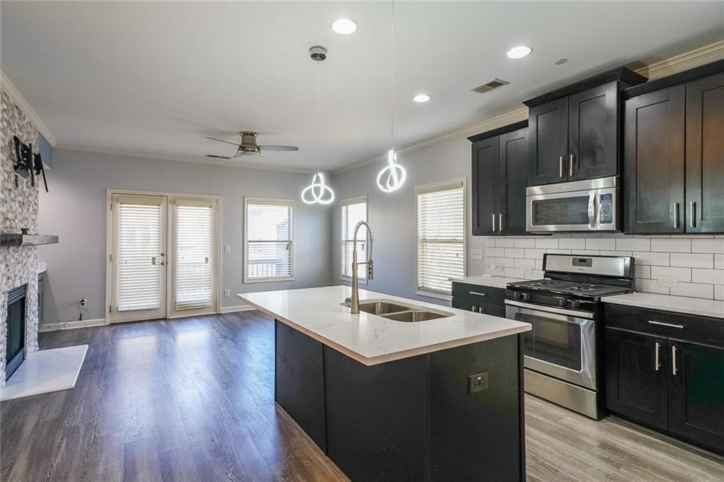 Kitchen with a stone fireplace, appliances with stainless steel finishes, light wood-type flooring, and tasteful backsplash
