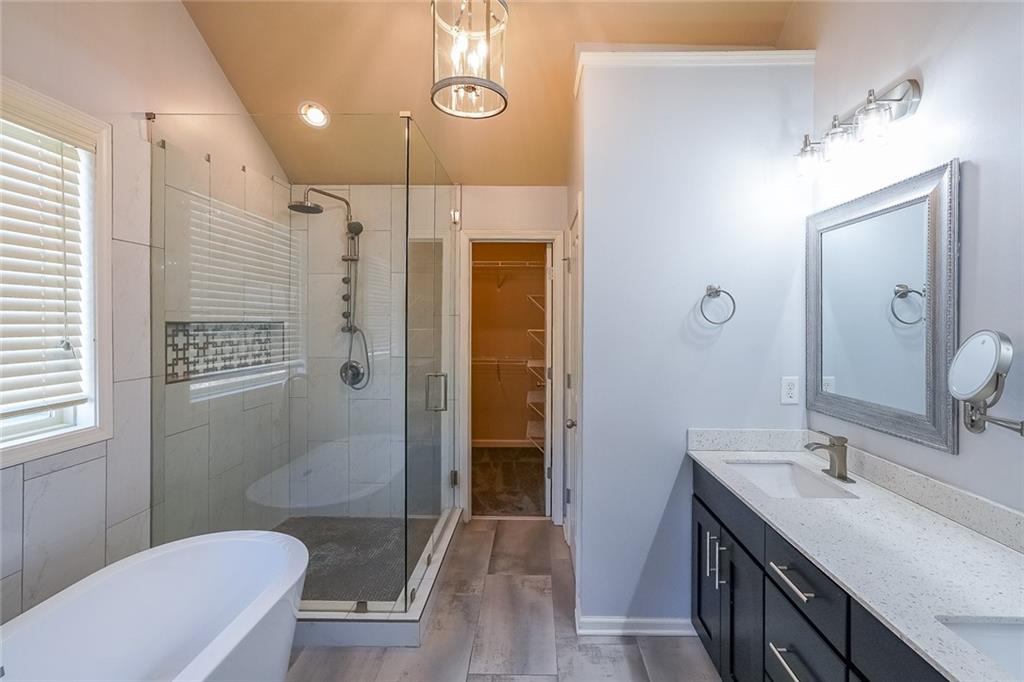 Bathroom with a wealth of natural light, double sink vanity, plus walk in shower, and wood-type flooring
