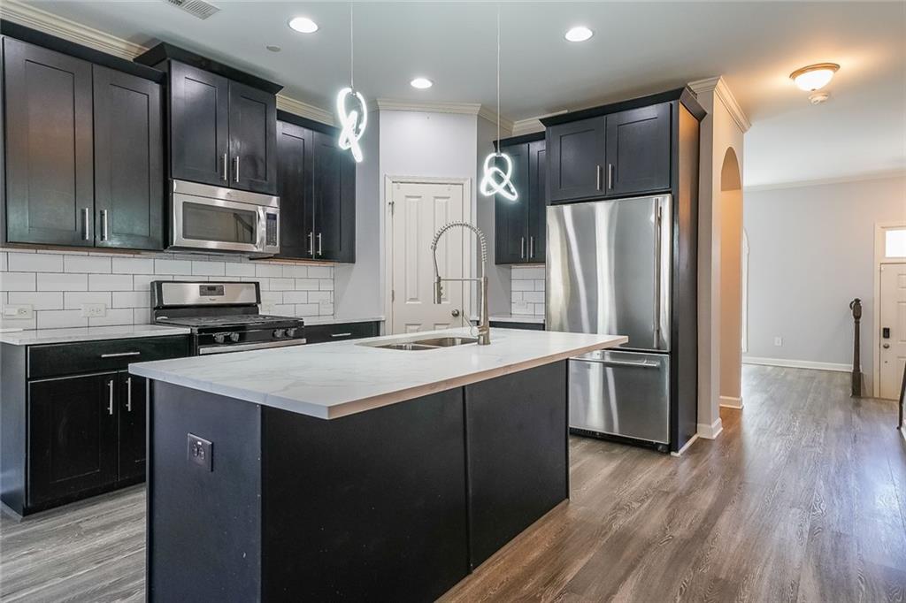 Kitchen featuring a kitchen island with sink, tasteful backsplash, hardwood / wood-style floors, stainless steel appliances, and decorative light fixtures