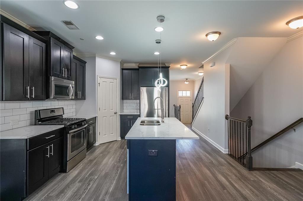Kitchen with dark wood-type flooring, stainless steel appliances, decorative light fixtures, and tasteful backsplash
