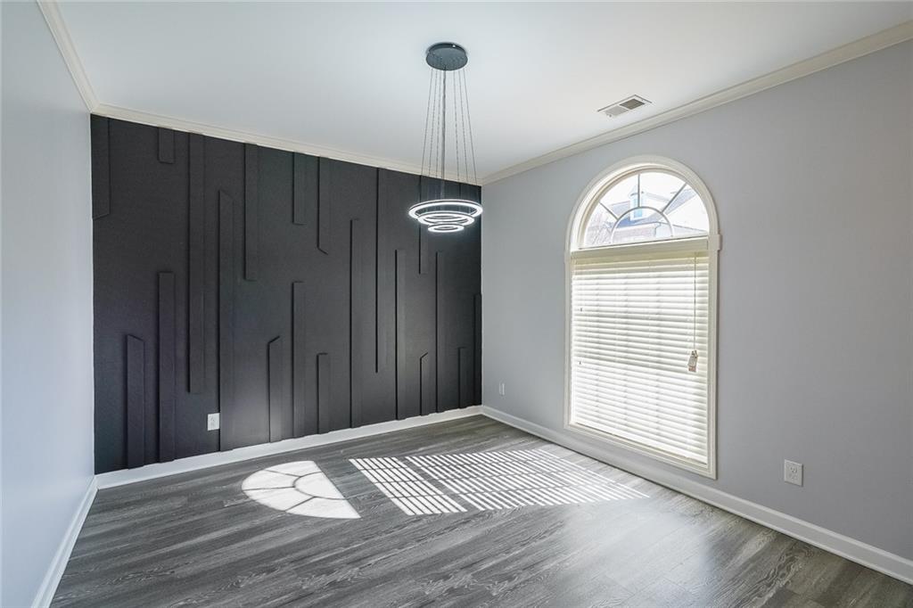 Unfurnished room featuring dark wood-type flooring, a notable chandelier, and crown molding