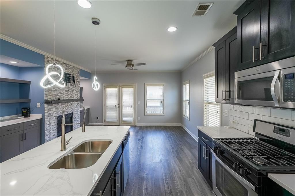 Kitchen with stainless steel appliances, a stone fireplace, dark hardwood / wood-style floors, decorative light fixtures, and ceiling fan
