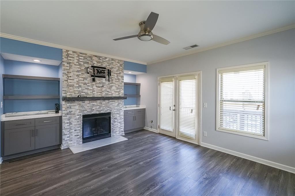 Unfurnished living room with dark hardwood / wood-style flooring, a stone fireplace, crown molding, built in features, and ceiling fan
