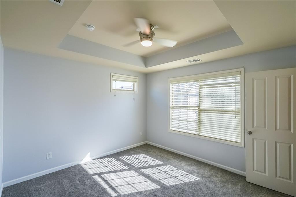 Carpeted empty room with ceiling fan and a raised ceiling