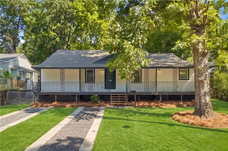 Elevated home featuring a covered front porch with decorative railings, a manicured lawn, and a gravel driveway