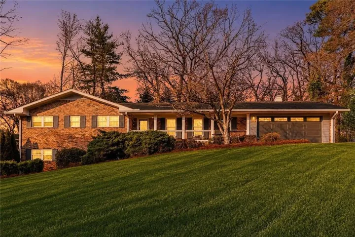 Brick exterior with dark shutters, an attached garage, and a covered front porch featuring white columns